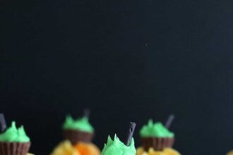 A mini halloween cupcake frosted with orange frosting and topped with a mini peanut butter cup and green icing meant to look like a cauldron