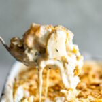 A spoon lifting a serving of cheesy chicken hashbrown casserole from a baking dish.