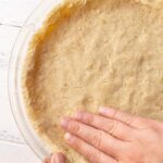 A hand pressing a shortbread graham cracker pie crust into the pie plate.