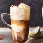 an alcoholic root beer float in a clear glass with a handle.