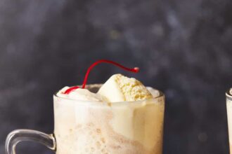 an alcoholic root beer float in a clear glass with a handle.