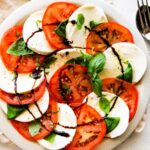 A caprese salad on a plate with sliced mozzarella cheese, sliced tomatoes, fresh basil, and a drizzle of balsamic vinegar.