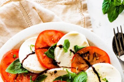 A caprese salad on a plate with sliced mozzarella cheese, sliced tomatoes, fresh basil, and a drizzle of balsamic vinegar.