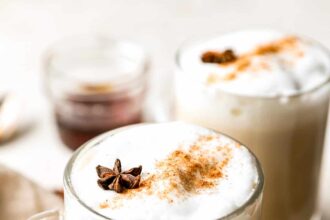 Two mugs of chai latte with cinnamon and star anise.