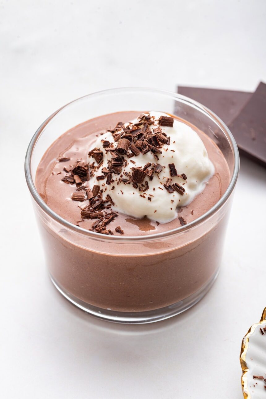 Chocolate protein pudding in a glass cup topped with whipped cream and shaved chocolate.