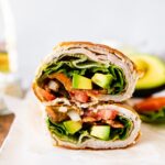 Two sections of a cottage cheese wrap with turkey, tomato, avocado, lettuce and onion visible inside the wrap.