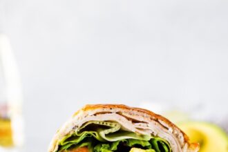 Two sections of a cottage cheese wrap with turkey, tomato, avocado, lettuce and onion visible inside the wrap.