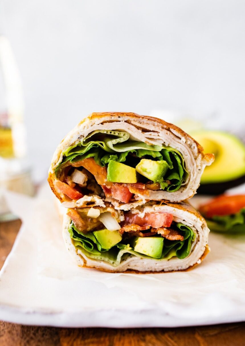 Two sections of a cottage cheese wrap with turkey, tomato, avocado, lettuce and onion visible inside the wrap.