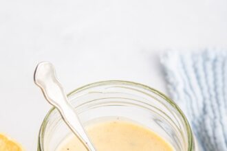 A creamy honey mustard dressing in a glass jar with a metal spoon inside the jar.