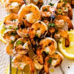 Grilled shrimp covered in herbs and spices on metal skewers.