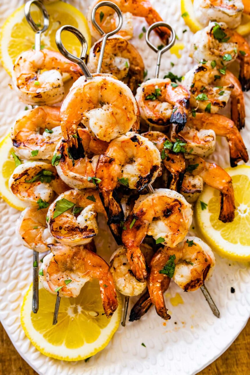 Grilled shrimp covered in herbs and spices on metal skewers.