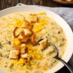 A bowl of instant pot broccoli cheddar soup topped with croutons with a spoon.