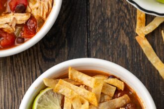 Overhead view of a bowl of chicken tortilla soup garnished with lime wedges and crispy tortilla strips.