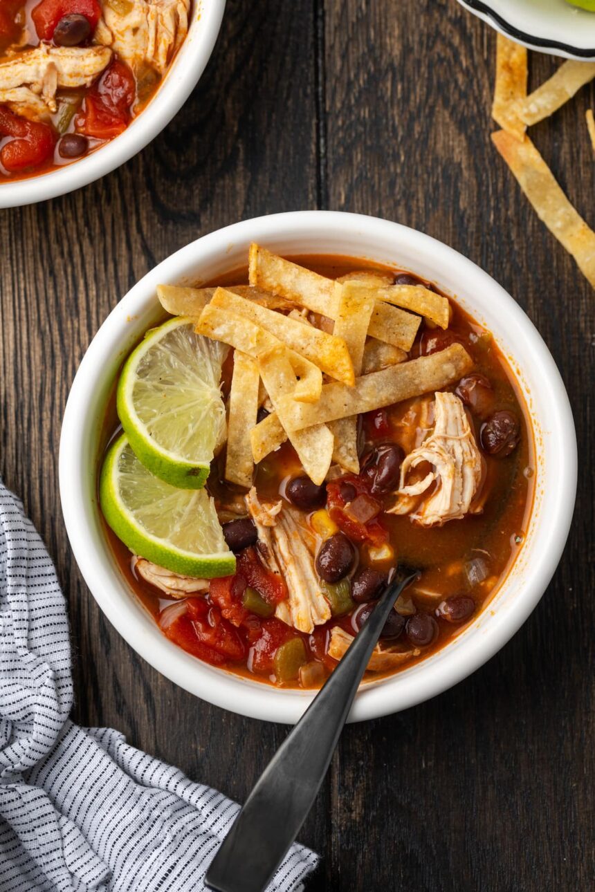 Overhead view of a bowl of chicken tortilla soup garnished with lime wedges and crispy tortilla strips.