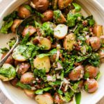 A no mayo potato salad in a large bowl with potatoes, spinach, sun dried tomatoes and fresh herbs.