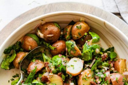 A no mayo potato salad in a large bowl with potatoes, spinach, sun dried tomatoes and fresh herbs.