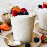 Overnight oats with yogurt in a glass cup, on a small plate, and topped with fresh berries.