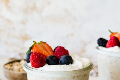 Overnight oats with yogurt in a glass cup, on a small plate, and topped with fresh berries.