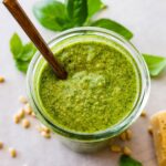 Overhead photo of a glass jar full of homemade pesto with a spoon in the jar.