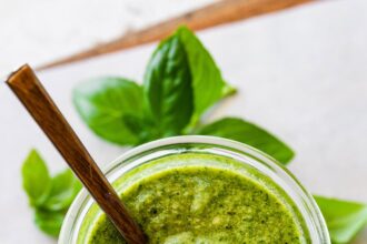 Overhead photo of a glass jar full of homemade pesto with a spoon in the jar.