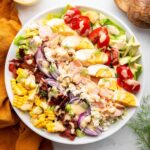 A salmon cobb salad in a bowl with fresh vegetables and a drizzle of a creamy honey mustard dressing.