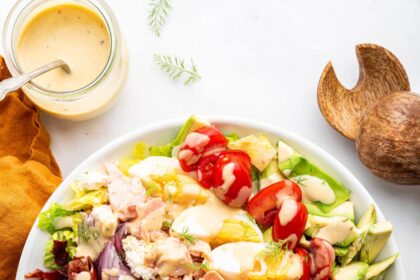 A salmon cobb salad in a bowl with fresh vegetables and a drizzle of a creamy honey mustard dressing.