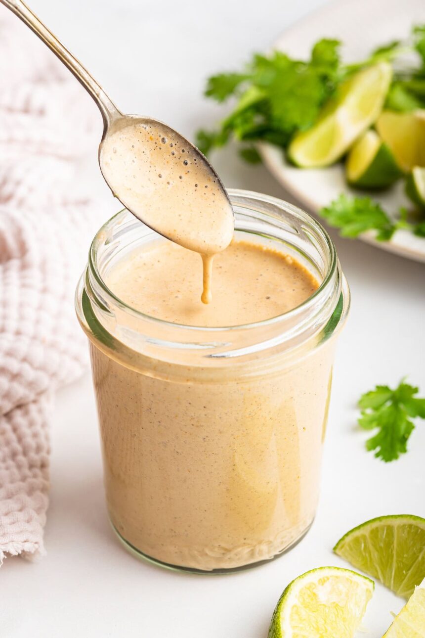 A glass jar filled with the creamy southwest dressing. A silver spoon is in the jar scooping out some of the dressing.