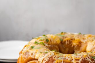 Taco monkey bread topped with melted cheese on a white plate, next to a bowl of shredded lettuce.