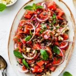 A watermelon salad with crumbled feta cheese, fresh basil, balsamic vinegar, and red onions.