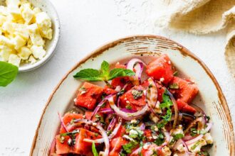 A watermelon salad with crumbled feta cheese, fresh basil, balsamic vinegar, and red onions.