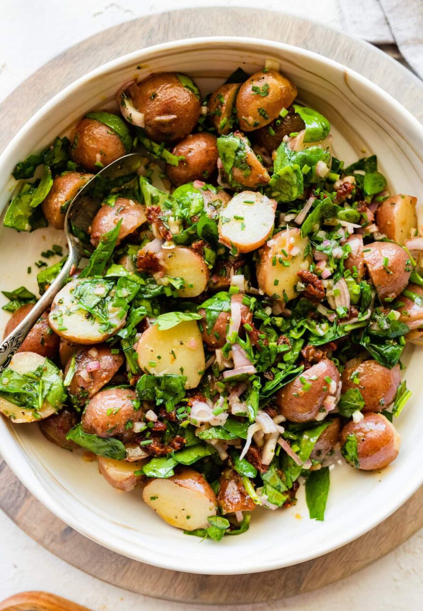 A no mayo potato salad in a large bowl with potatoes, spinach, sun dried tomatoes and fresh herbs.