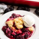 Blackberry Cobbler served up with a scoop of ice cream on top of it on a white plate.