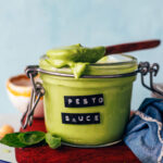 Spoonful of creamy pesto sauce resting on top of a jar with more sauce in it