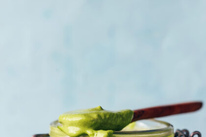 Spoonful of creamy pesto sauce resting on top of a jar with more sauce in it