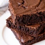 Three squares of the most amazing brownies stacked on top of each other on a white plate