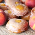 Peach pie donuts stacked next to fresh peaches