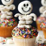 A halloween cupcake topped with a skeleton made from marshmallows and white chocolate covered pretzels