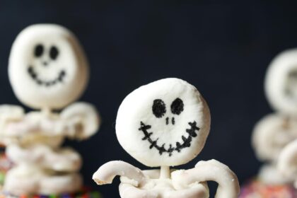 A halloween cupcake topped with a skeleton made from marshmallows and white chocolate covered pretzels