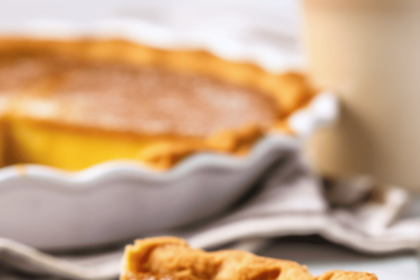 A clean slice of chess pie on a white plate with the rest of the pie in the background.