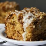 A slice of apple cake on a white plate topped with a thin layer of white glaze icing