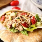 A crunchy chicken salad inside of a piece of pita bread on a table with cherry tomatoes