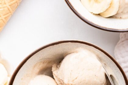 Three scoops of banana ice cream in a bowl with a metal spoon and two slices of banana.