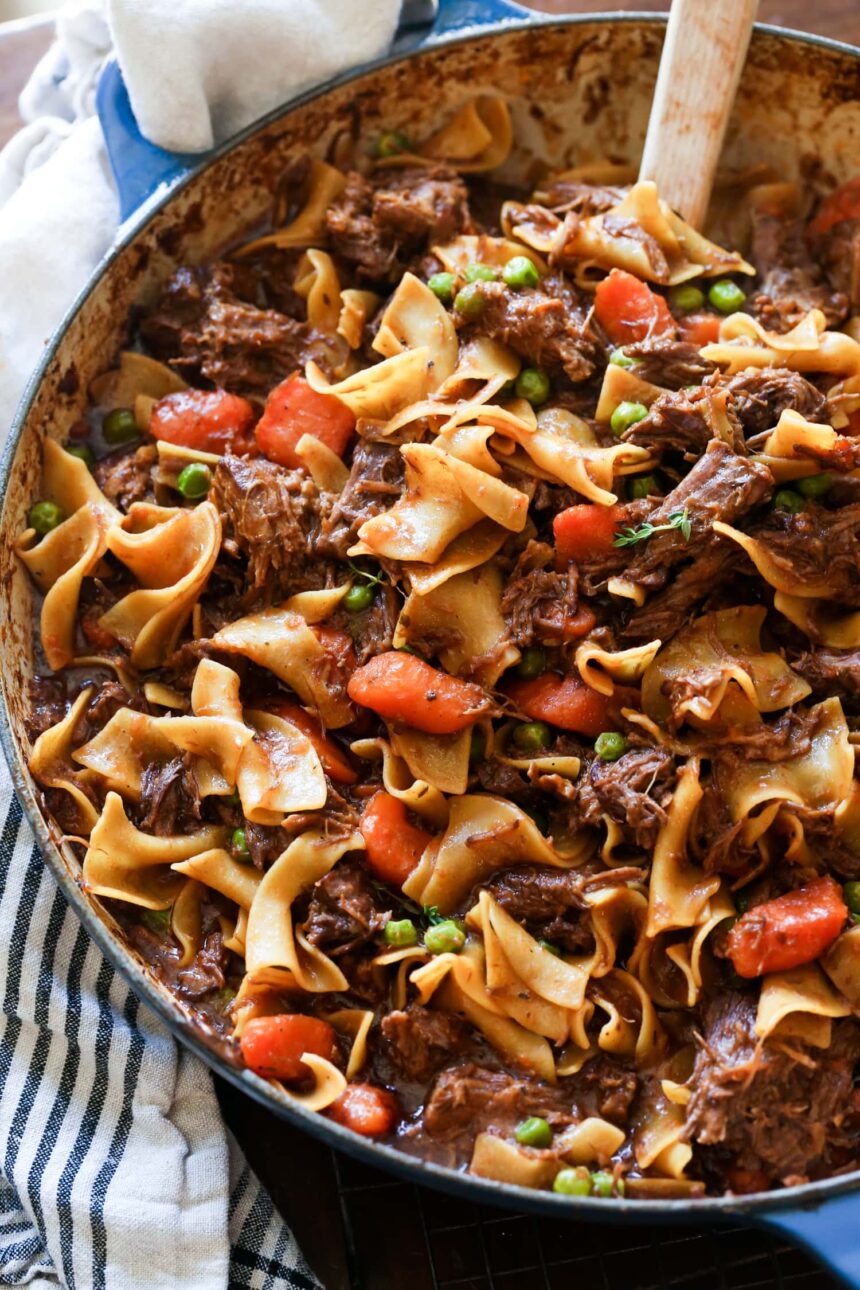 Beef and noodles cooked in a dish with carrots and peas