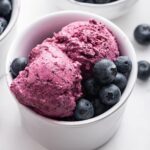 A few scoops of blueberry frozen yogurt in a small bowl with fresh blueberries inside the bowl.