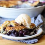 A piece of blueberry cobbler on a white plate with a scoop of ice cream