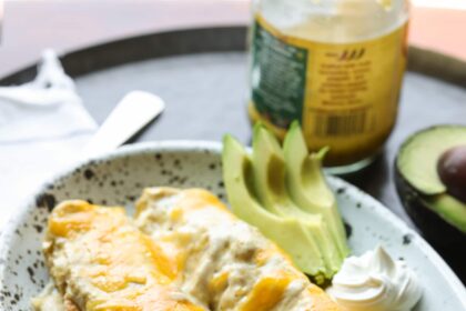 Chicken Enchiladas on a serving plate covered in melted cheese with avocado slices