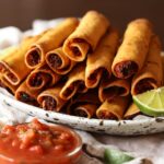 chicken taquitos fried golden brown on a plate with lime wedges