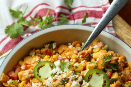 Spicy Frito corn salad topped with cotija cheese and sliced jalapeños in a large white salad bowl with a serving spoon.