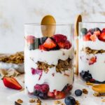 Two glass cups of fruit and yogurt parfaits. The cups are layered with fruit, yogurt, granola, then yogurt again and more fruit on top.