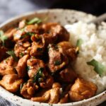 Ginger chicken served in a bowl over rice, garnished with fresh chopped coriander.